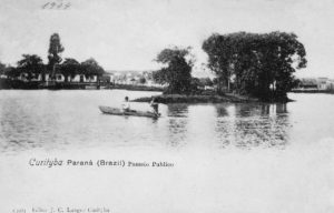 Curitiba - Postal em preto e branco que mostra uma canoa com duas pessoas no lago principal do Passeio Público, em 1904. Ao fundo, o engenho Bittencourt. Postal da Coleção Julia Wanderley. Acervo: Instituto Histórico e Geográfico do Paraná / Diretoria de Patrimônio Histórico, Artístico e Cultural / Fundação Cultural de Curitiba.